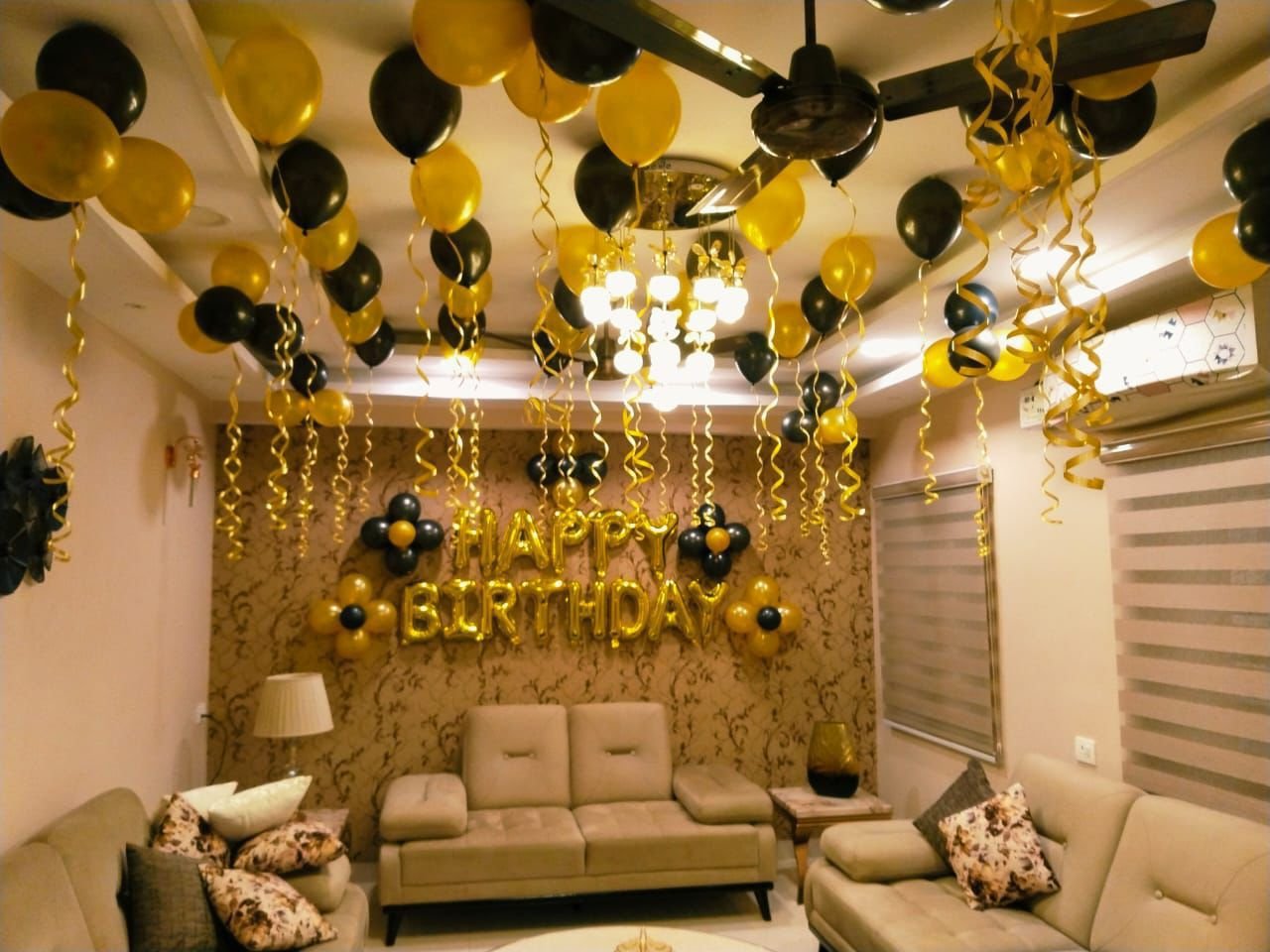 Black and gold birthday balloon decoration with a Happy Birthday backdrop in a living room